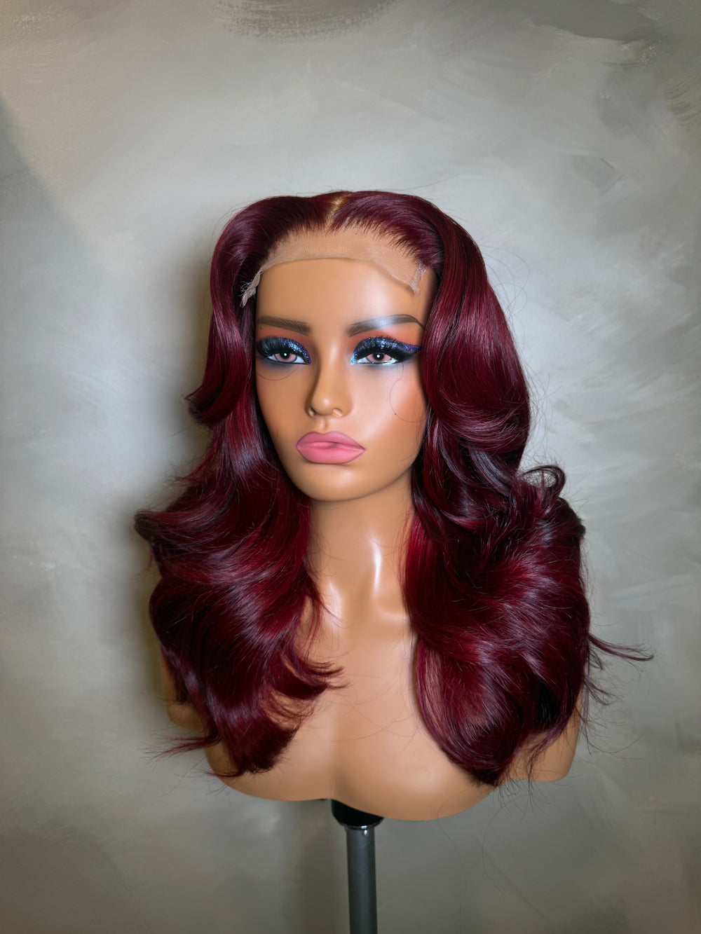 Mannequin head with burgundy wig on a neutral background