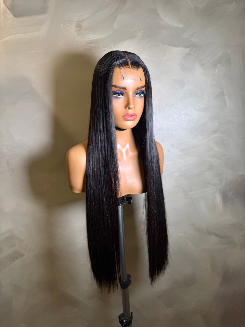 Black straight wig on a mannequin head against a neutral background